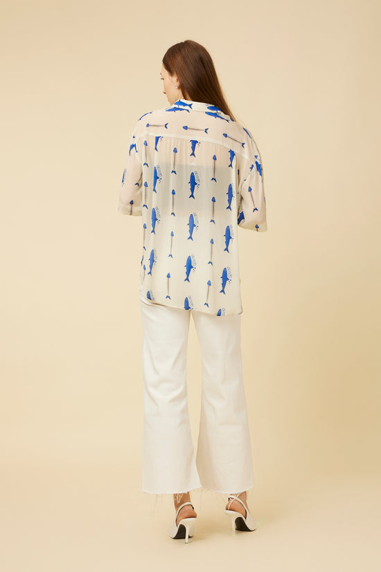 Back view of the Voyager Sheer Shirt, focusing on the sheer fabric and fish print, paired with elegant cream pants