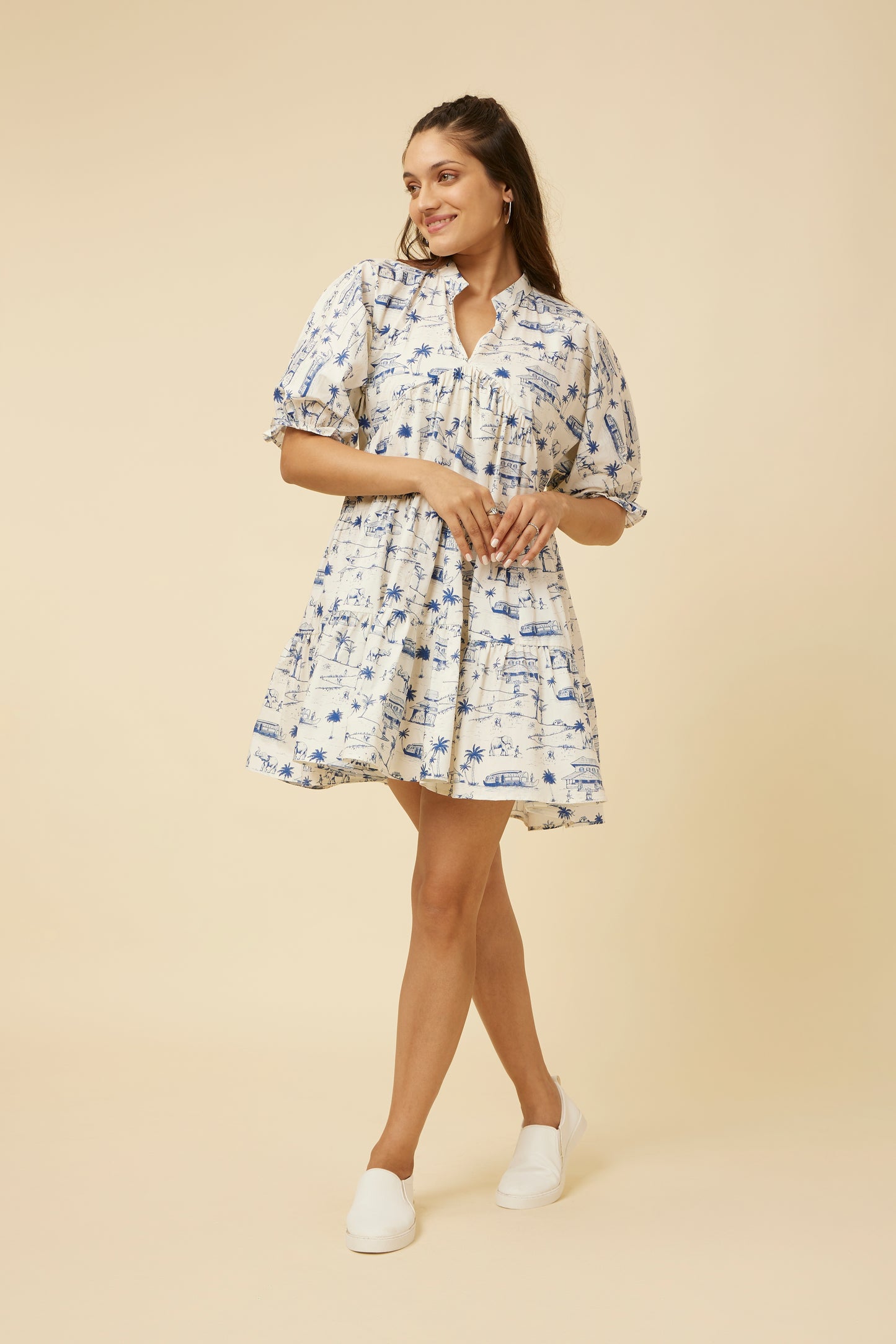 Model poses in the Homeland Dress, highlighting its whimsical print and tiered structure, complete with a comfortable yoke collar and casual footwear