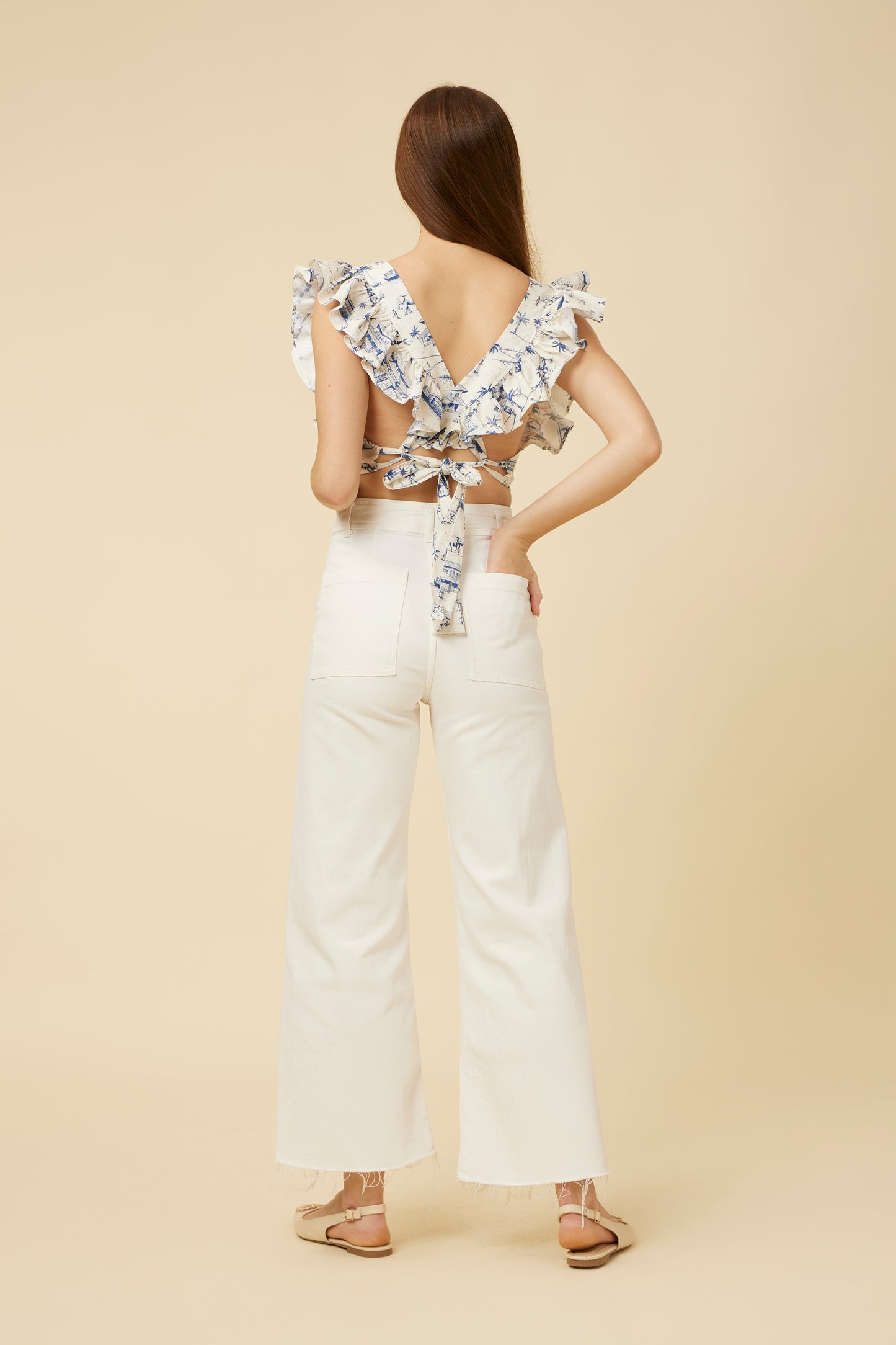 Back view of the Homeland Frill Crop Top showing the unique overlapping back frill and tie detail at the hem, styled with casual high-waist pants.